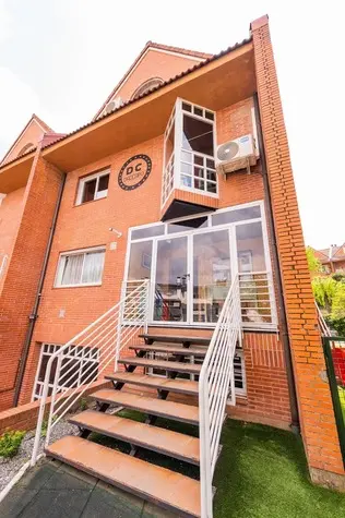 La casa de DACCAPO por fuera: fachada de ladrillo con el sello DC, escalera de madera y jardín.