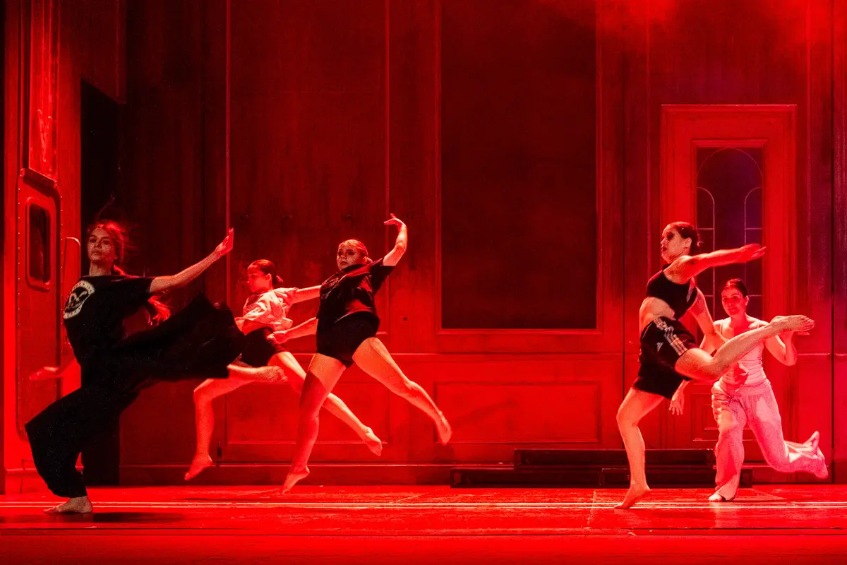 Bailarines saltan a la vez sobre un escenario bañado de luz roja.