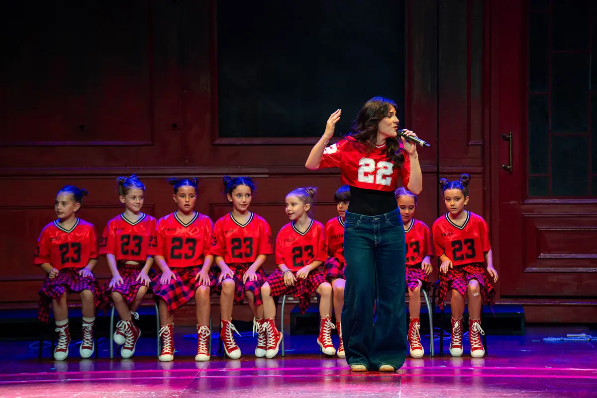 Una solista canta delante de un coro sentado con camisetas rojas.