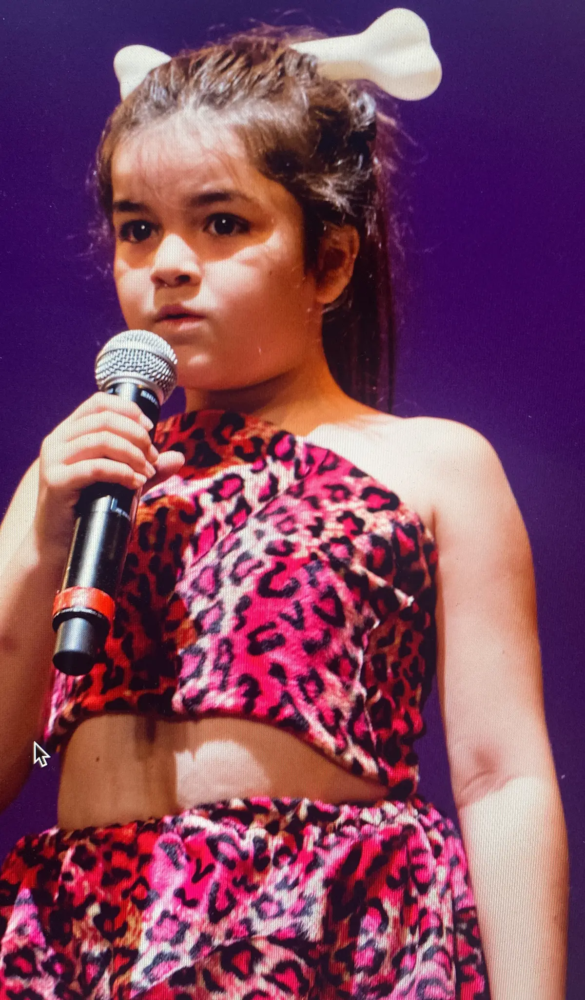 Foto de archivo: una niña con vestuario de leopardo canta con micrófono.