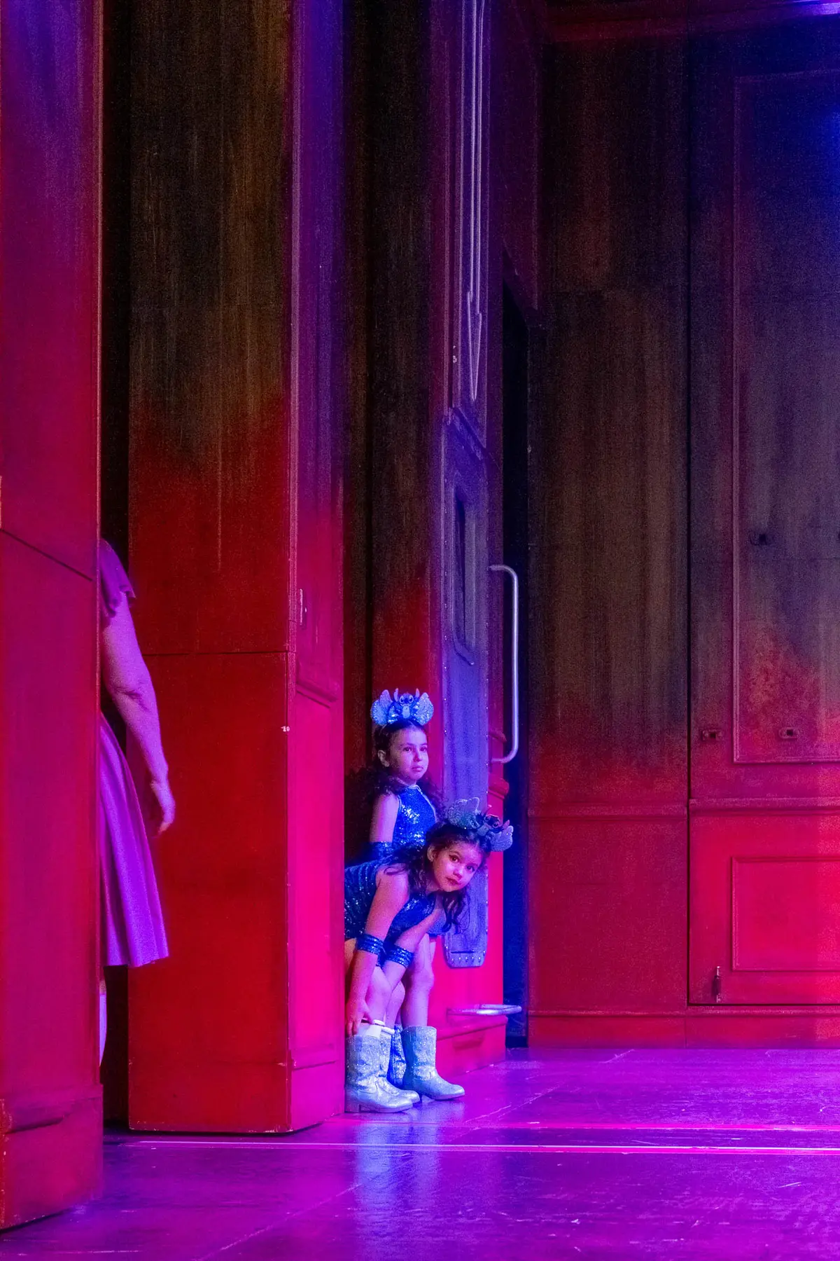 Dos alumnas pequeñas se asoman a escena desde una puerta del decorado.
